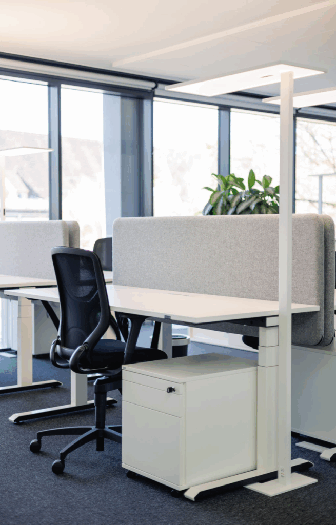Modern ausgestatteter Arbeitsplatz im Open Space des RITZ mit ergonomischem Stuhl, Sichtschutz und Tageslicht durch große Fensterfront.
