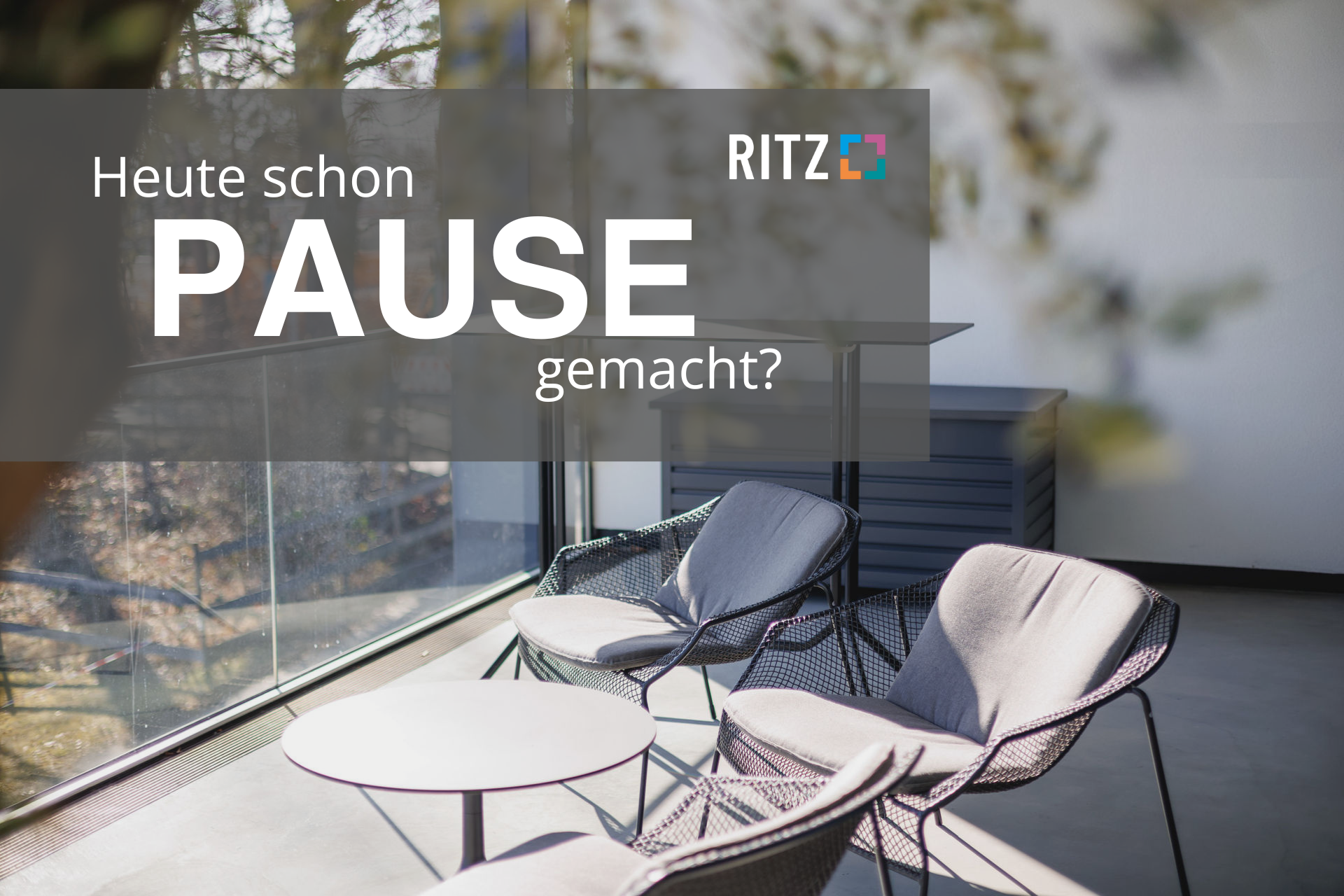 Sonnige Lounge-Ecke mit modernen Sesseln und Glastisch im RITZ, darüber der Schriftzug: „Heute schon PAUSE gemacht?“.
