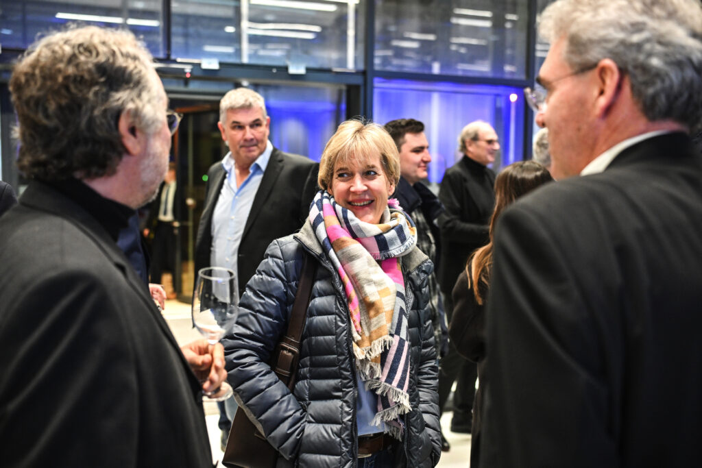 Mehrere Gäste im Gespräch bei der Veranstaltung "Beispielhaftes Bauen", eine Frau in der Bildmitte lächelt, umgeben von Männern in dunkler Kleidung.