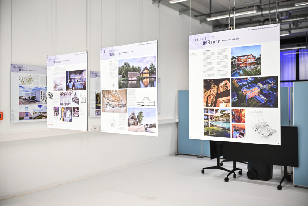 Ausstellungstafeln mit prämierten Projekten der Auszeichnung „Beispielhaftes Bauen“, aufgehängt in einem modernen Innenraum.