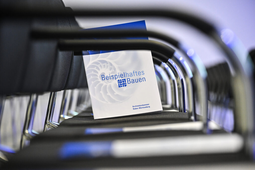Broschüre zur Auszeichnung „Beispielhaftes Bauen“ liegt auf einem Stuhl zwischen Stuhlreihen.