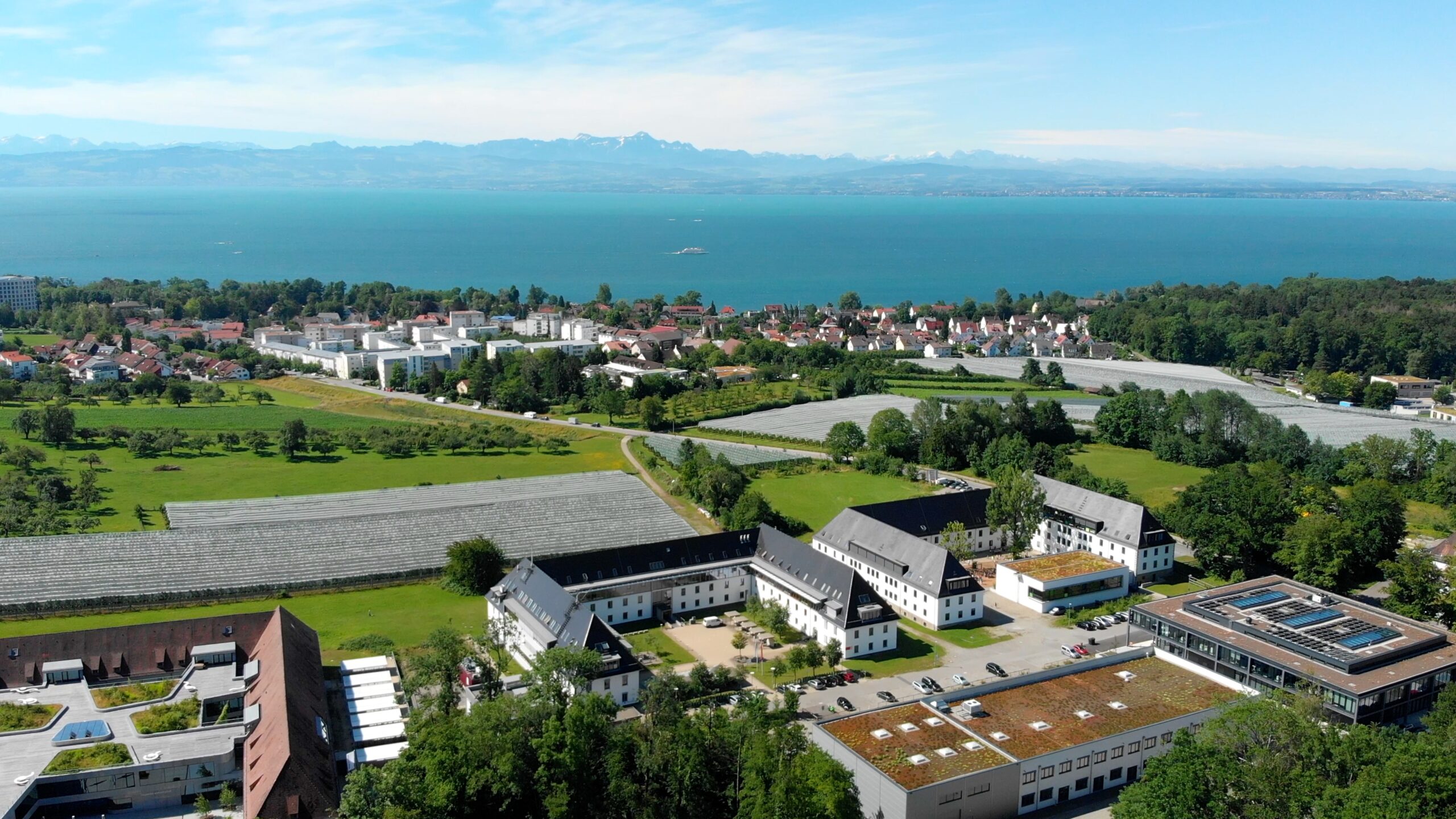 Luftaufnahme des RITZ-Areals in Friedrichshafen mit Blick auf Bodensee, Stadtgebiet und Alpenpanorama im Hintergrund.
