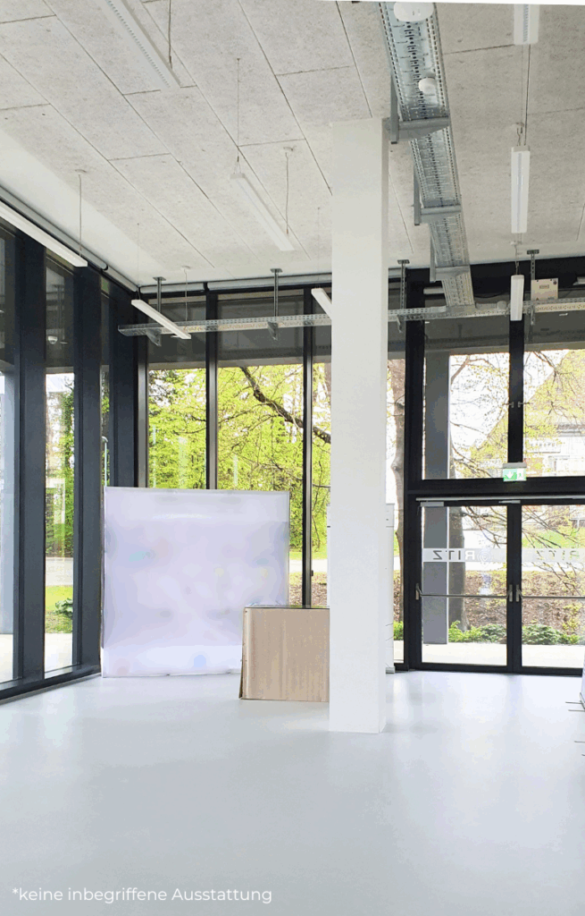 Großer, heller Showroom mit hohen Fenstern und Sicht auf grüne Außenfläche, minimal möbliert mit einem abgedeckten Tisch und Roll-Up.