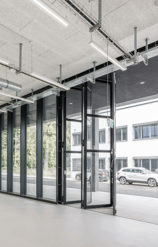 Blick von innen auf den Innovation Space mit offener Glasfaltwand und Sicht auf den Parkplatz.