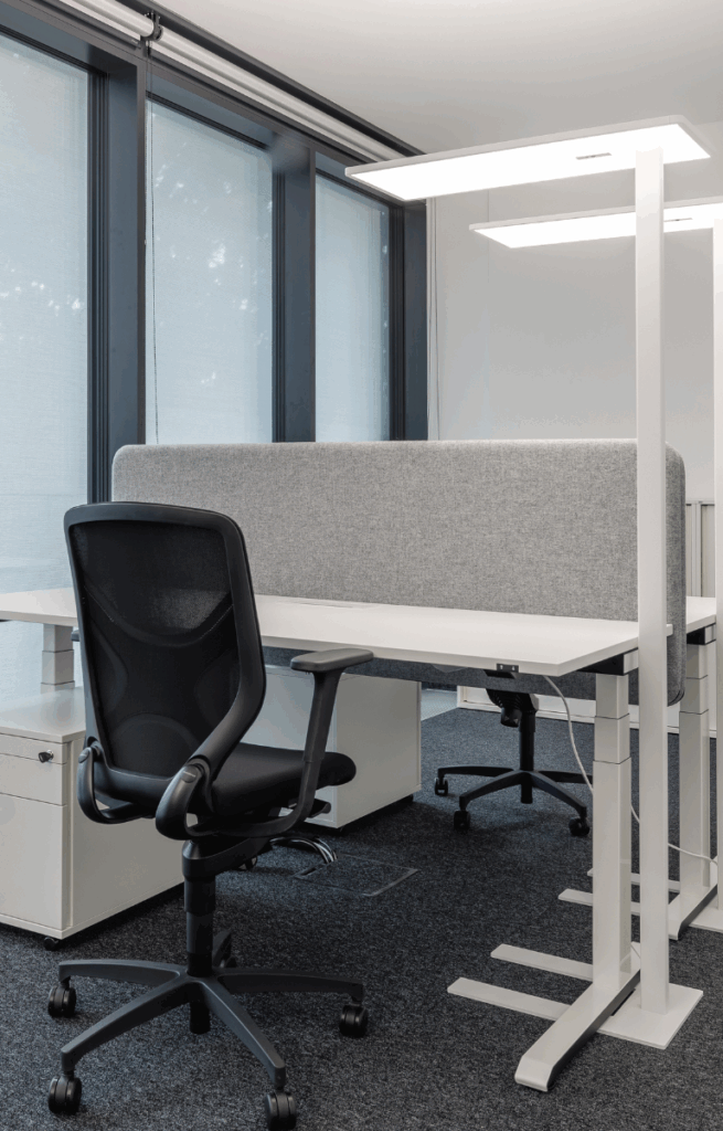 Modern eingerichteter Einzelarbeitsplatz mit höhenverstellbarem Schreibtisch, ergonomischem Stuhl und Akustikpaneel im RITZ Friedrichshafen.