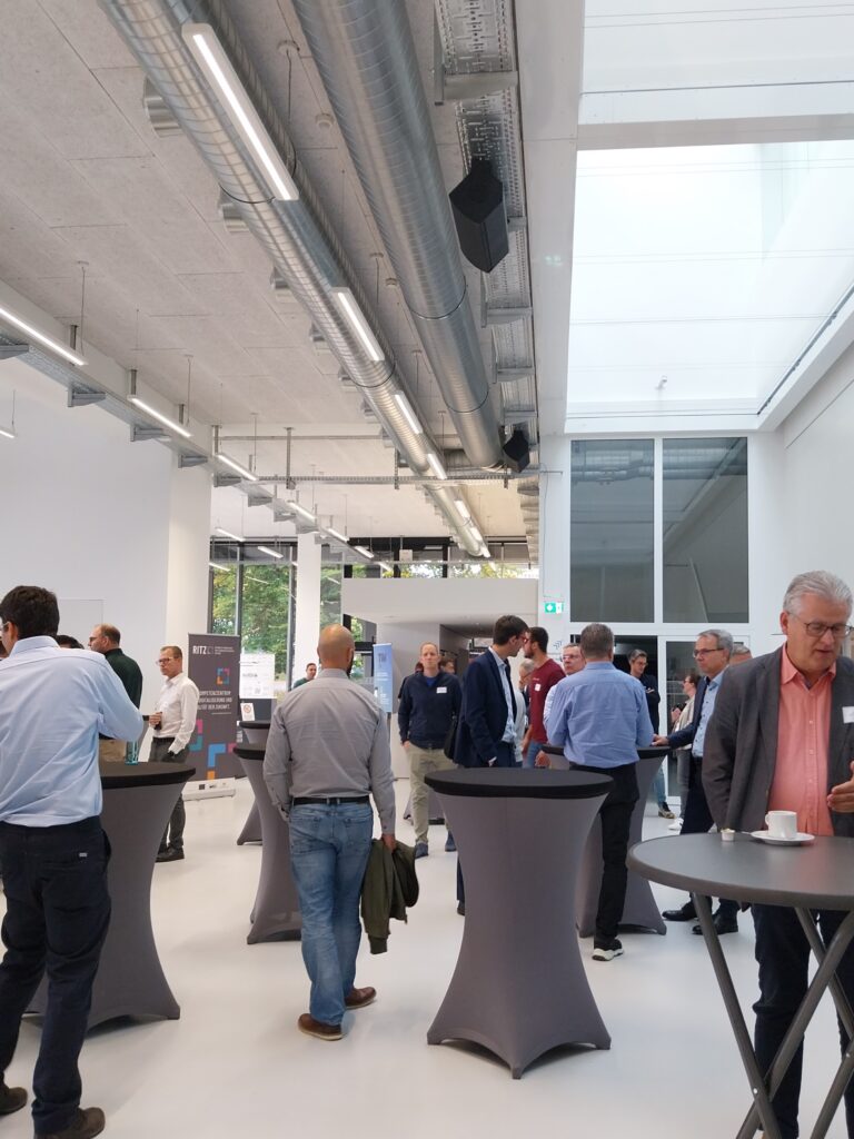 Menschen im Austausch während einer Netzwerkpause im RITZ Innovationszentrum. Stehtische, Tageslicht und moderne Architektur schaffen Raum für Gespräche.