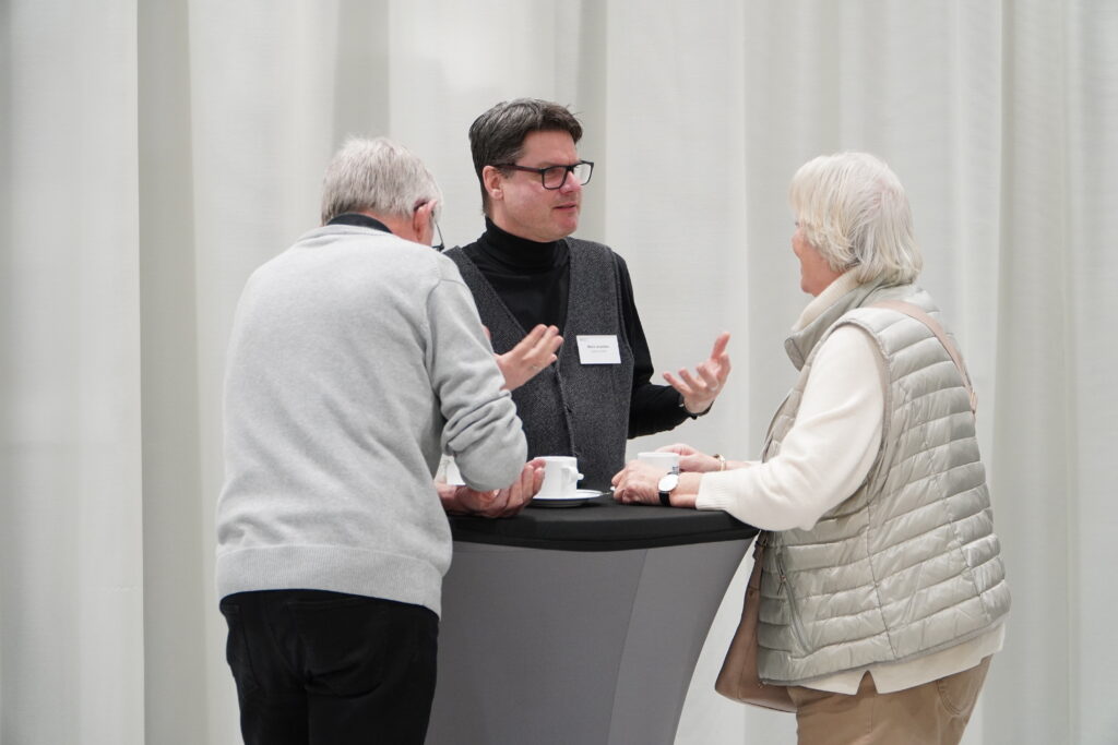 Drei Personen stehen bei Kaffee an einem Stehtisch im RITZ Friedrichshafen und führen ein angeregtes Gespräch beim Breakfast & Brainfood.