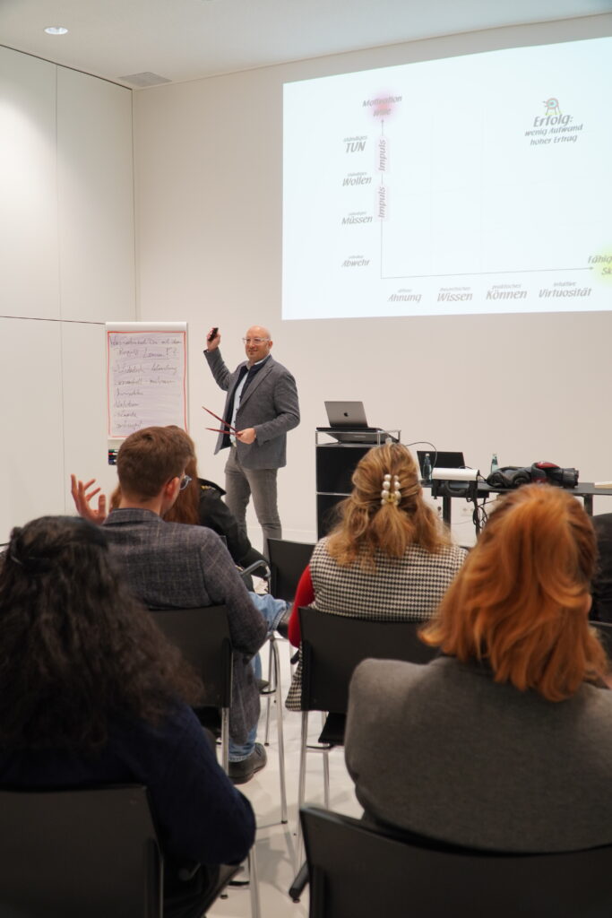 Philipp Gotterbarm steht während seines Vortrags bei ‚Breakfast & Brainfood‘ vor einer Projektion und einem Flipchart und spricht zu den Teilnehmenden im RITZ Friedrichshafen.