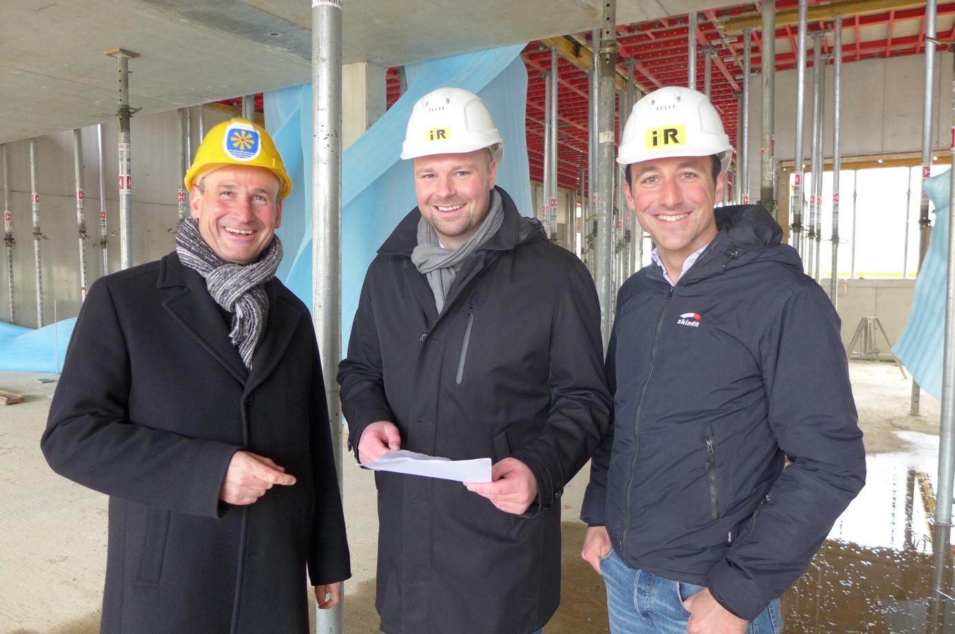 Architekt Harald Betting vom Bau- und Liegenschaftsamt des Bodenseekreises, RITZ-Geschäftsführer Marian Duram und Simon Bickel, Projektleiter des Generalübernehmers I+RB Industrie- und Gewerbebau, stehen mit Bauhelmen in einem Rohbau des RITZ Innovationszentrums.