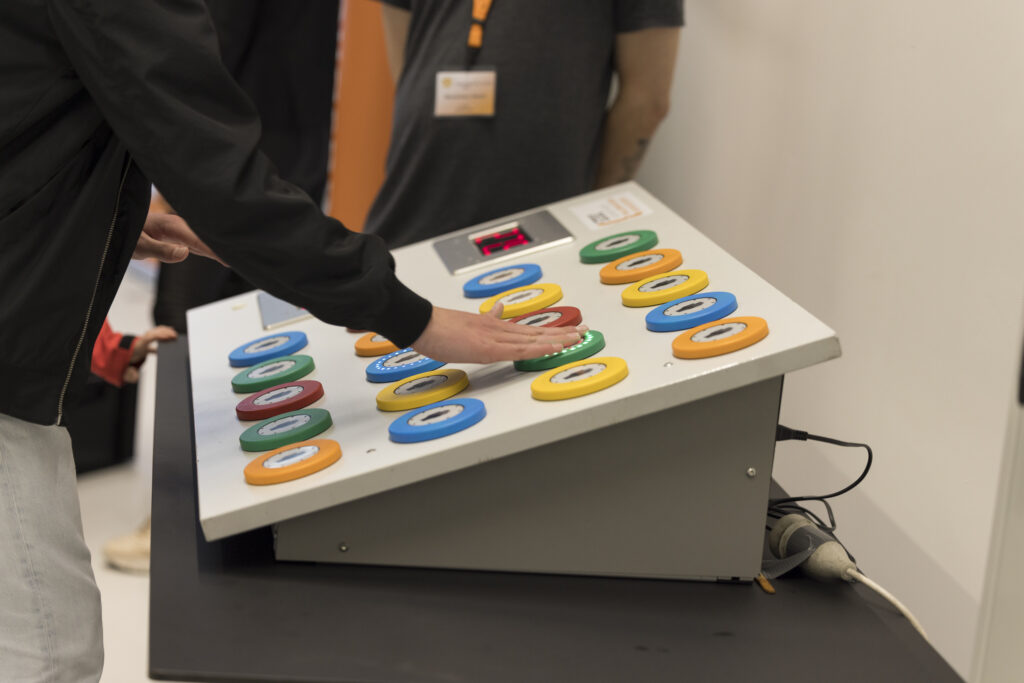 Interaktives Reaktionsspiel bei der Langen Nacht der Technik und Innovation (LNTI): Eine Person schlägt auf ein leuchtendes Feld eines Spieltisches mit bunten Tasten. Die Anzeige oben zeigt die verbleibende Zeit. Das Spiel fördert Reaktionsgeschwindigkeit und Koordination – Technik zum Anfassen für Jung und Alt.