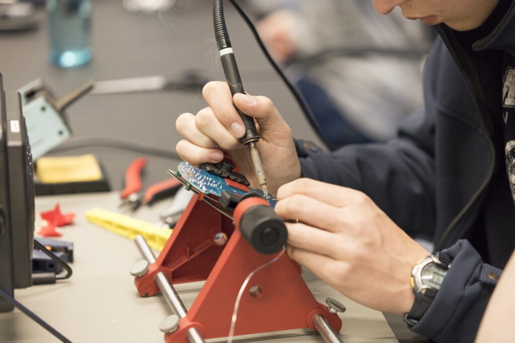 Junger Mensch lötet bei der Langen Nacht der Technik und Innovation (LNTI) konzentriert an einer Platine. Im Vordergrund ist die Lötstation zu sehen, im Hintergrund liegen Werkzeuge bereit. Technik wird hier greifbar – praxisnah und hands-on.