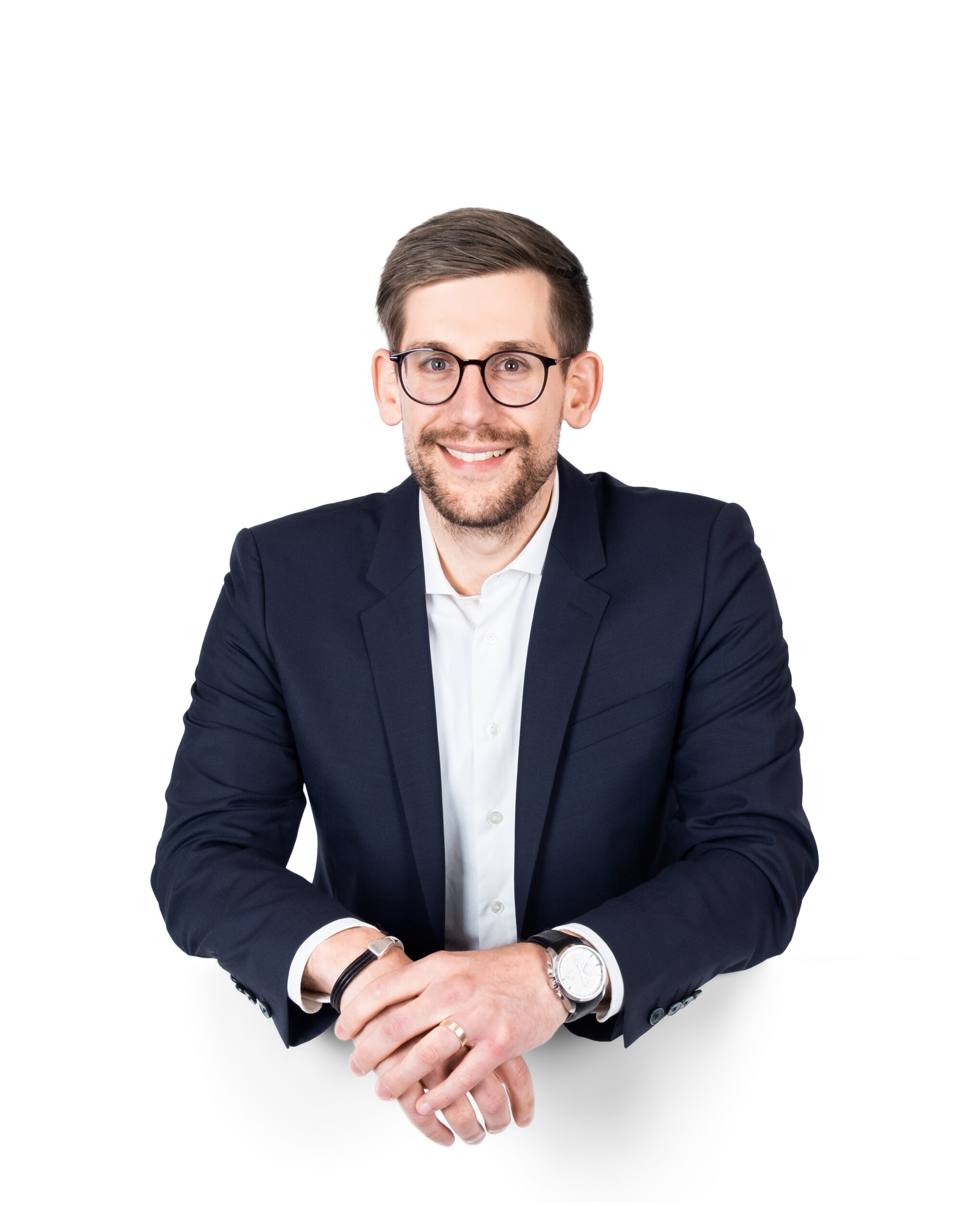Porträt von Sascha Schmidt, einem jungen Mann mit Brille, dunklem Sakko und weißem Hemd, der freundlich lächelnd in die Kamera schaut.