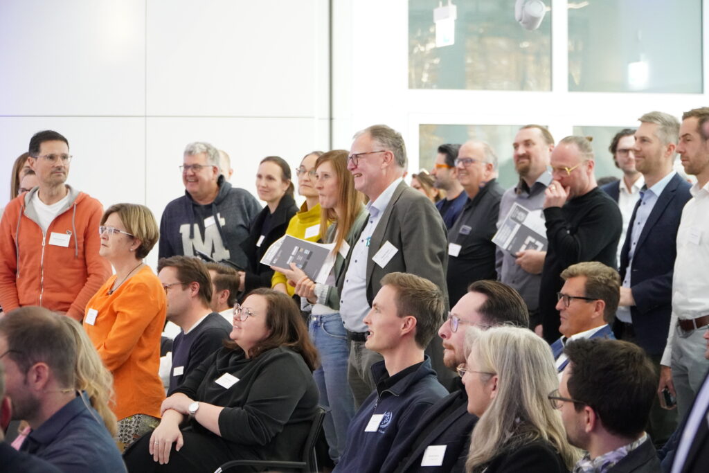 Teilnehmende stehen bei der Veranstaltung „Wer nicht innoviert, verliert“ im RITZ auf, um auf Fragen im Plenum zu reagieren.