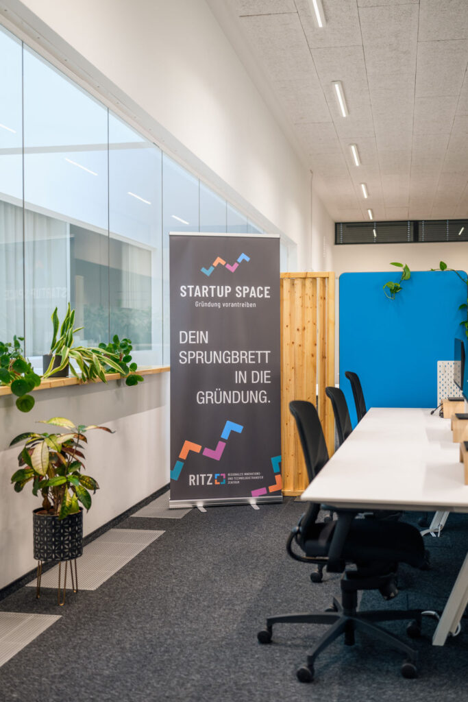 Roll-up „Startup Space, Dein Sprungbrett in die Gründung“ im RITZ-Büroraum mit Schreibtischen und Pflanzen